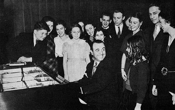 man at piano with students gathered around